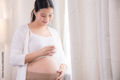 Pregnant mother drinking milk while touching belly, reflecting maternity care, nutrition, wellness, healthcare support, happiness and positive lifestyle during prenatal stage with family preparation Free Download Pregnant mother drinking milk while touching belly, reflecting maternity care, nutrition, wellness, healthcare support, happiness and positive lifestyle during prenatal stage with family preparation - GFXLoad