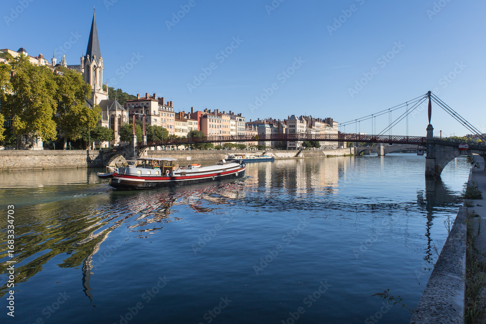Fototapeta premium La Saône avec un bateau de croisière et vue sur l'église Saint-georges du vieux Lyon, la colline de Fourvière et les quais de Saône en été