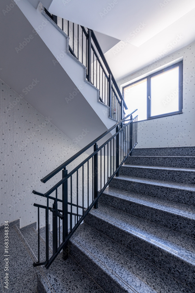 Obraz premium Modern stair case between floors. Stairs with metallic rail in modern building. Interior of a contemporary apartment or office building. Architecture and real estate background.