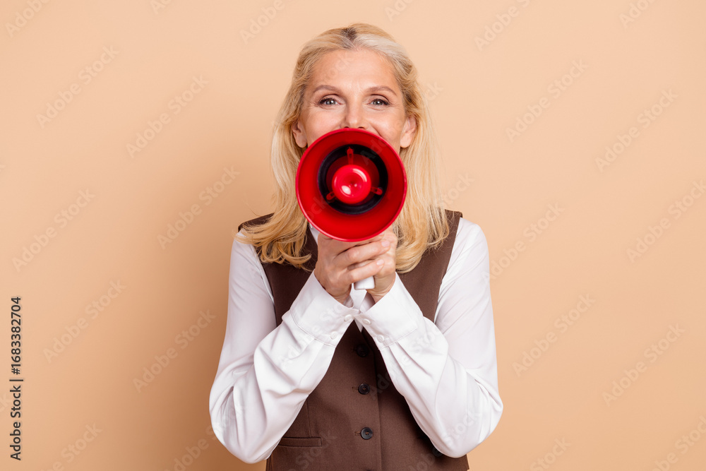 Obraz premium Smiling middle-aged businesswoman with megaphone posing against beige background, representing leadership and communication concepts