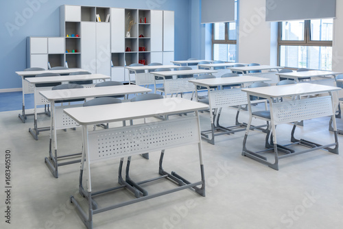Empty bright classroom with modern desks and chairs. Educational interior with furniture ready for lessons. Photo