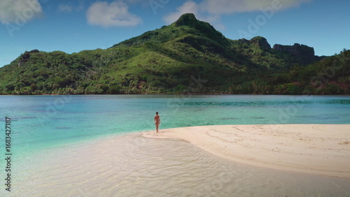 Woman wearing a bikini is enjoying a peaceful walk on the beach of a tropical island with lush green mountains in the background