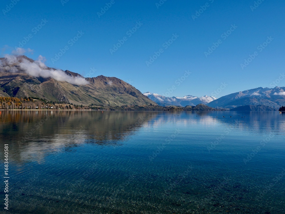 Fototapeta premium June 2025: Lake Tekapo with snow-capped mountains, autumn trees, and Church of the Good Shepherd under blue sky. Scenic view taken in South Island, New Zealand.