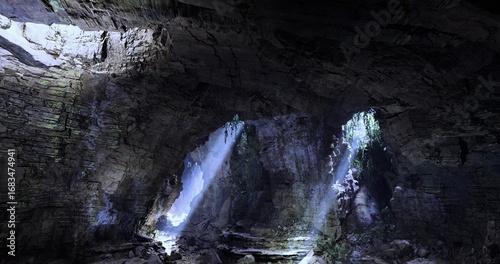 Obraz na plátně Dramatic rays of sunlight pierce dark cave openings, highlighting the rugged stone walls