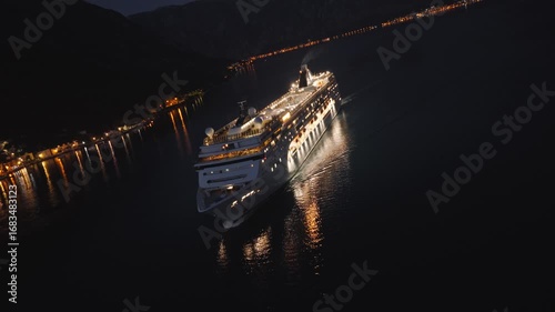 Unique aerial footage of a luxury cruise liner sailing through Kotor Bay near Perast, Montenegro, during blue hour. The drone performs a spiraling orbit with camera roll rotation