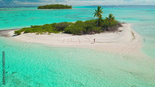 Young female on wild island waving hands ask to save her. Aerial view small tropical island beach, turquoise coral reef. Woman need rescue. Word HELP written on sand beach. Aerial view drone flight