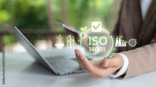 Businesswoman holding ISO 14001 certification icon with laptop, symbol of environmental management system, sustainable business, eco industry and corporate responsibility.