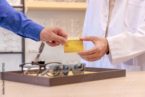Close up shot of payment by credit card between an ophthalmologist and a client in optical shop