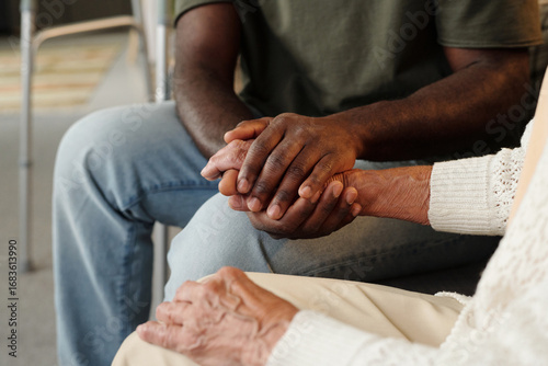 Black man holding hands with senior Caucasian woman, offering comfort and support, close up on hands showing intergenerational connection and emotional care in supportive setting