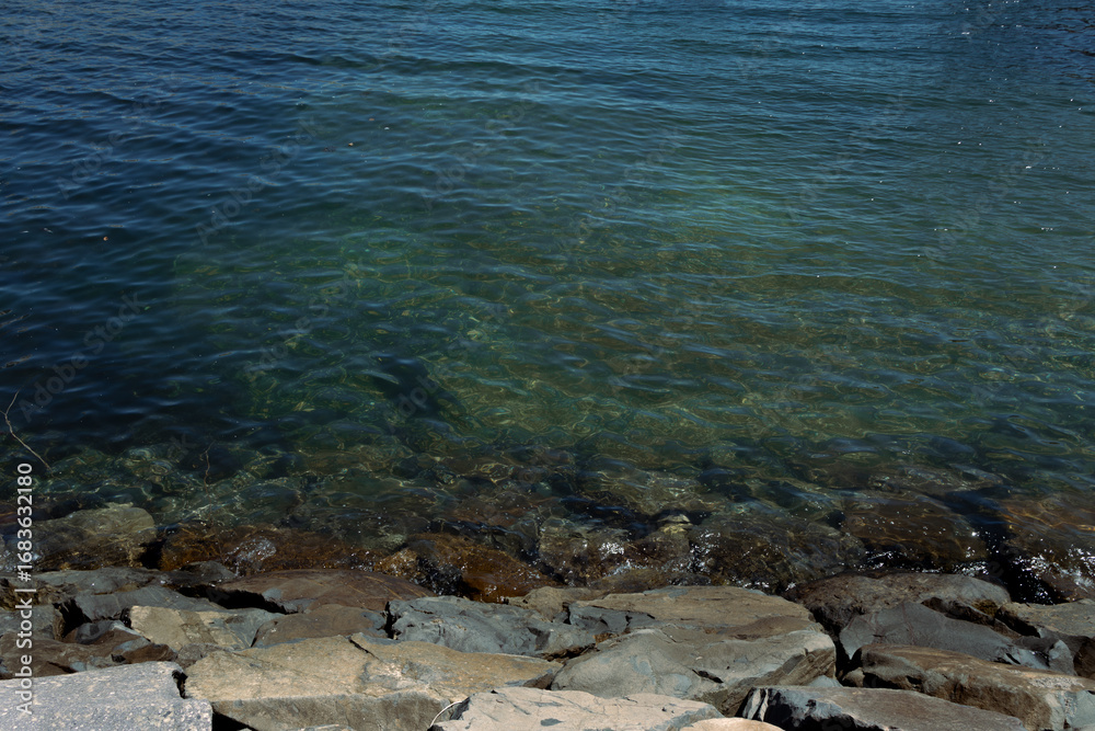 Obraz premium Clear water of a lake with visible rocks on the shore. Natural background with blue and green transparent water and stone coastline.