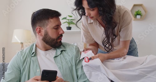 Couple confrontation over lipstick stain evidence. She shows the shirt; he holds a smartphone and denies an affair as suspicion, jealousy, and argument erupt. Concept: infidelity and distrust.