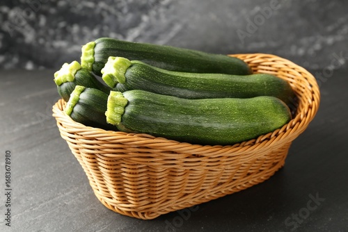 Fotografie Fresh ripe zucchinis in wicker basket on black table, closeup