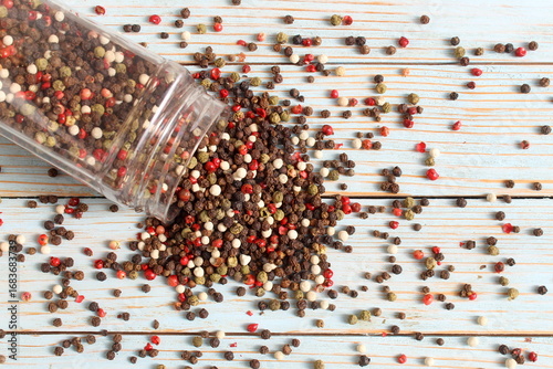  On a wooden table lies an overturned transparent plastic container containing different types of peppercorns.