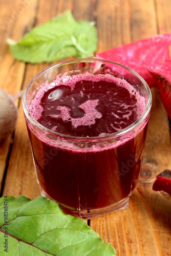 There is a glass of freshly squeezed beetroot juice on the wooden table.