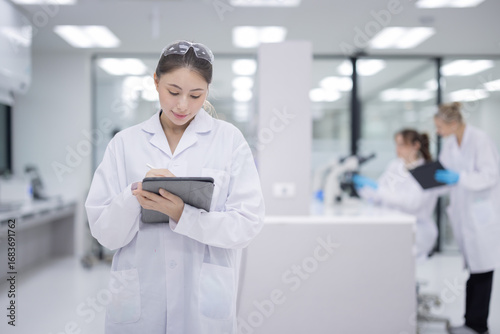 Femail scientist wearing a lab coat holding a tablet and smiling in a modern laboratory