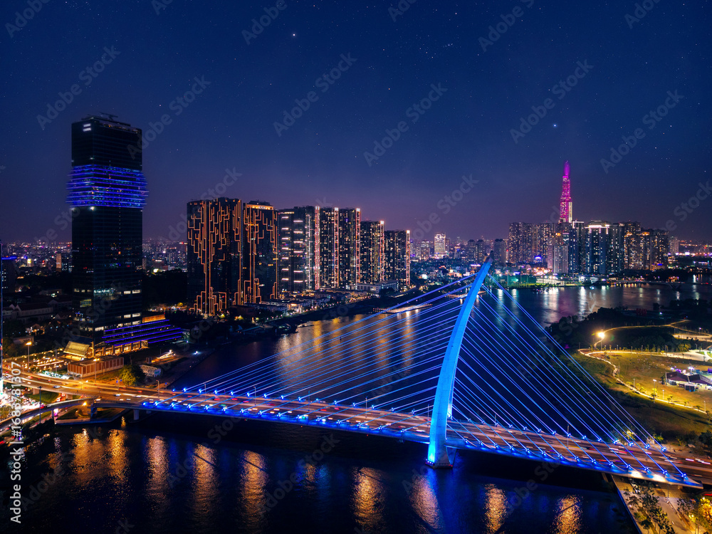 Fototapeta premium Aerial view Ho chi minh city and Saigon river in Vietnam, neon illuminated of bridge and business center with skyscrapers with night stars