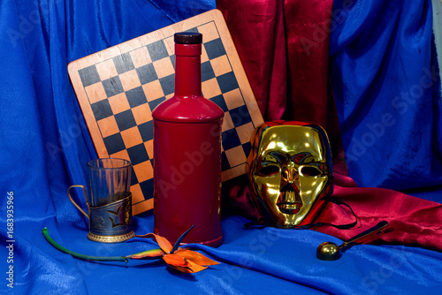 
still life with a red bottle and a golden mask