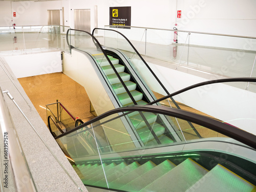 Multiple escalators connect different airport floors with glass railings, yellow floor below, and empty bright modern architecture