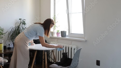 A woman cleans and dusts her house with a rag
