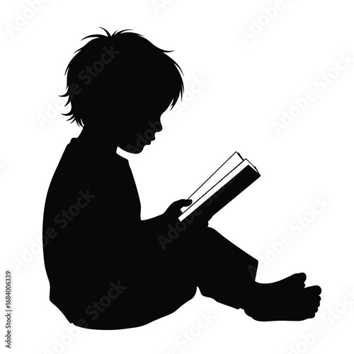Silhouette of a young boy sitting and concentrating intently while reading a book open in his hands