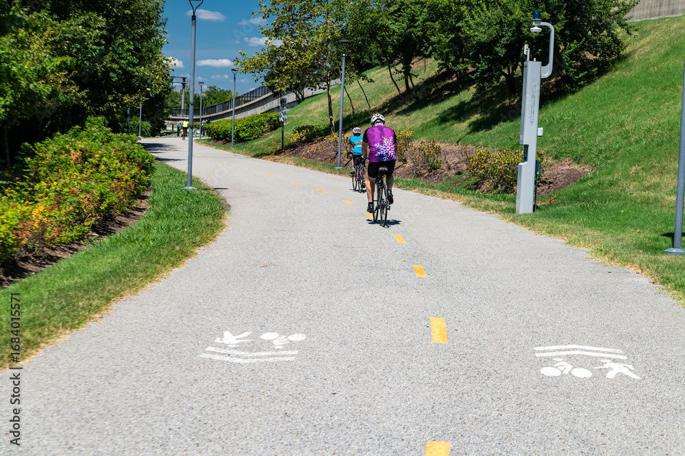 Fototapeta premium Bike path surrounded by trees and modern infrastructure. Cyclists on the path.