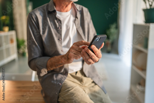 Fotografi Senior man using smart phone at home: browsing internet and staying connected
