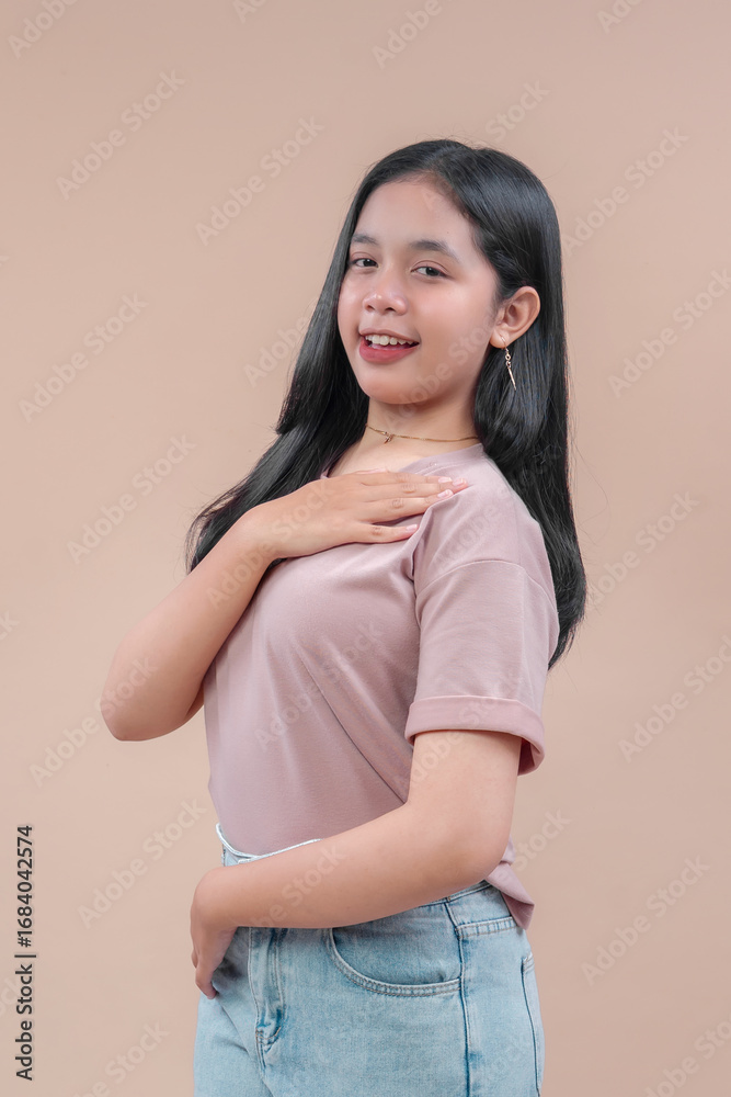 Obraz premium Asian young woman with long black hair wearing casual t-shirt and denim jeans, smiling with one hand on chest, showing confident and friendly pose against beige background.