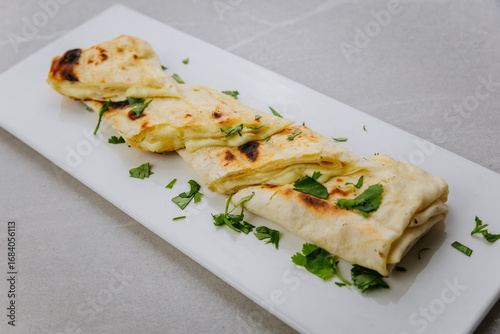 Grilled lavash rolls with melted cheese and herbs on a white ceramic plate