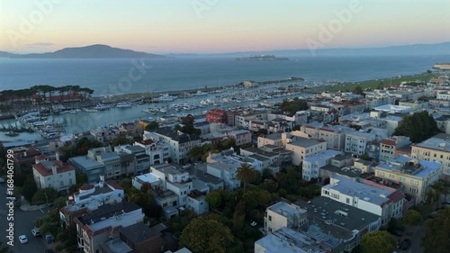 Breathtaking aerial shot over stunning scenery of the San Francisco marina, featuring vibrant city life and the tranquil waters during a picturesque sunset, with Alcatraz island prison in a distance.