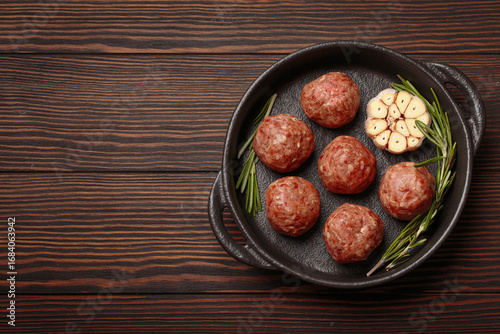 Raw meatballs seasoned with garlic and rosemary ready to be cooked in a cast iron pan, on a dark wooden table