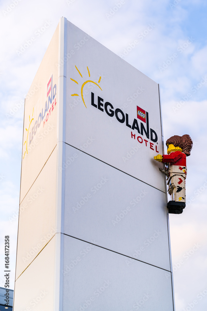 Obraz premium A colorful LEGO figure is seen climbing the Legoland Hotel Resort sign during a beautiful sunset in Billund Denmark, highlighting the playful spirit of this family-friendly destination