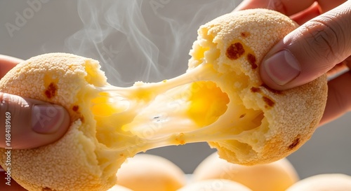 Hand Tearing Open a Hot Pão de Queijo, Showing Stretchy Melted Cheese.
