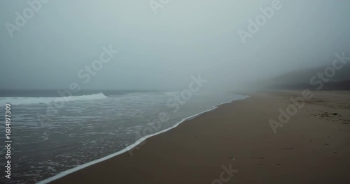 Clip start showing gentle waves lapping misty sandy beach, with foam line advancing and receding