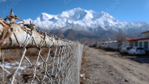 Rusty chainlink fence foregrounds snow-capped mountains