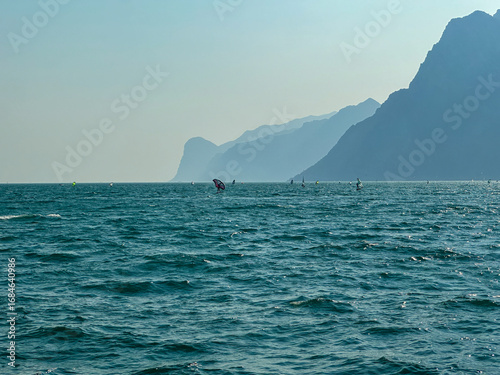 Canvas-taulu Windsurfers and foilers enjoy the strong wind on the choppy waters of Lake Garda, framed by the majestic Italian Alps in the background