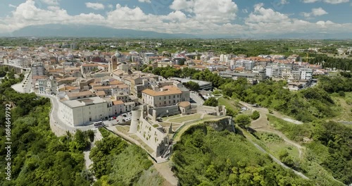 Aerial view of Ortona's ancient castle nestled atop a verdant hill overlooking the city's terracotta rooftops and lush green landscape, Ortona, Abruzzo, Italy.
