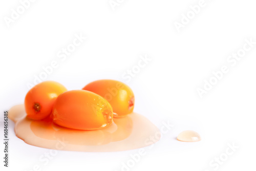 Three sea buckthorn berries in oil on white background, copy space, natural skincare concept, real photo.