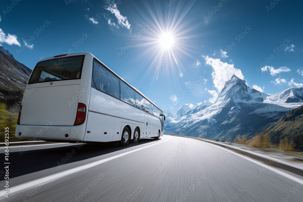 Obraz premium White coach bus driving on a sunny mountain road with snow-covered peaks under a clear blue sky