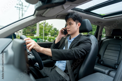 Asian businessman talking on phone, working inside a car while driving. 
