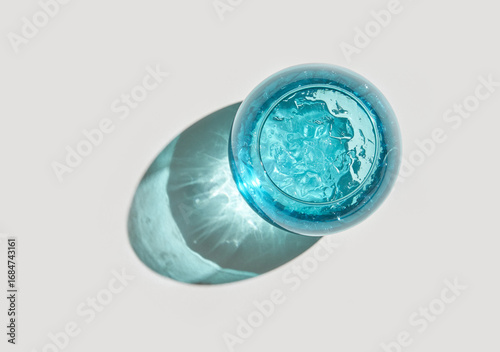 Top view of refreshing blue drink with ice in glass casting shadow on light background.
