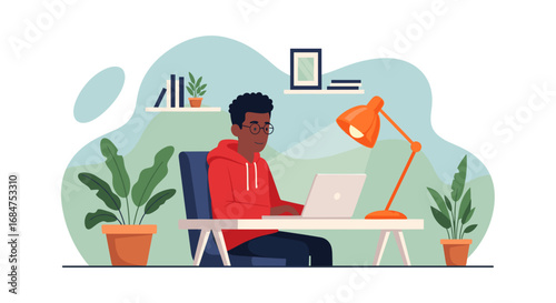 Young Black man in glasses and a red hoodie works on a laptop at a modern home office desk with plants. Illustrates remote work, study, or digital lifestyle.