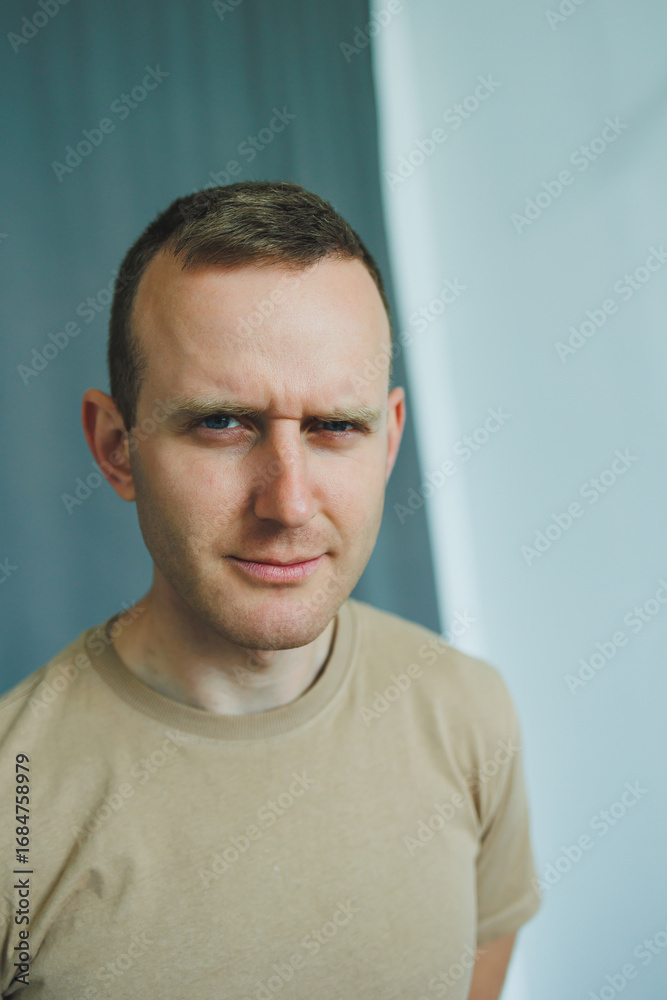 Obraz premium A confident young man in casual wear stands against a minimalist backdrop, showing his charming smile and relaxed pose. The image reflects creativity, modern masculinity, and youthful individuality