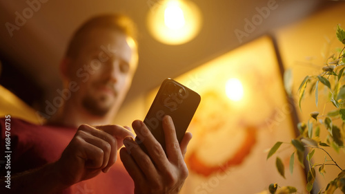Low angle view of man swiping on smartphone beside a anime maid girls poster