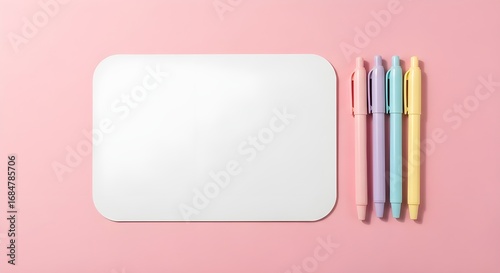 Four pastel colored pens arranged next to a blank white rounded rectangle on a pink background