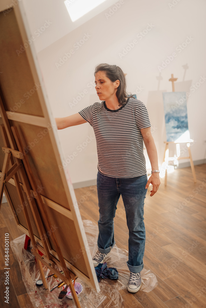Fototapeta premium Female artist evaluating her painting on canvas in art studio