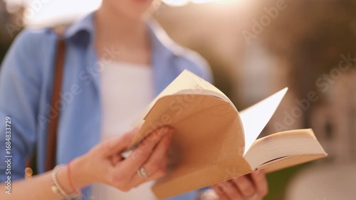 Close up of book in woman’s hands, pages flipping quickly outdoors in sunlight, study, reading, knowledge, education, inspiration, literature, peaceful lifestyle moment.