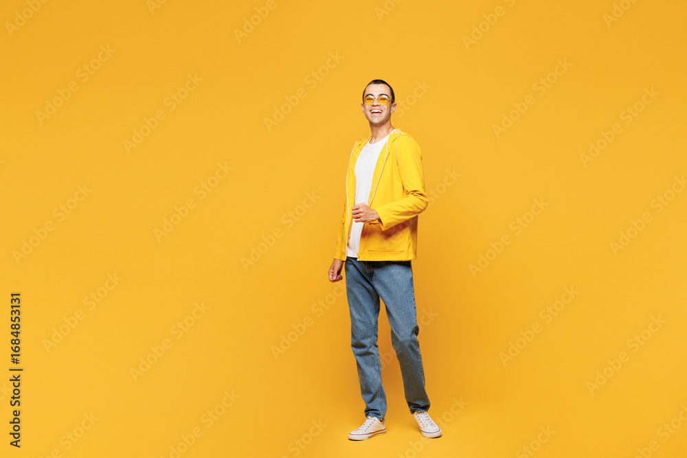 Fototapeta premium Full body young smiling fun happy cheerful positive middle eastern man wearing orange raincoat casual clothes stand look camera isolated on plain yellow background studio portrait. Lifestyle concept.