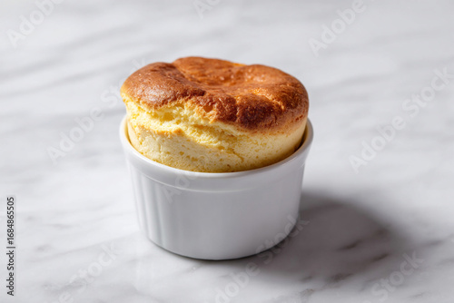 Cheese soufflé with golden crust in white ramekin. Minimalist presentation highlights airy texture and elegance of the dish
