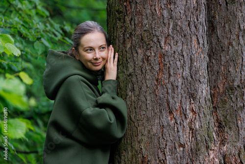 Woman enjoys nature while embracing a tree in a serene forest setting during daylight hours