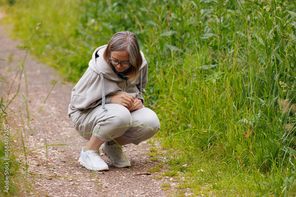 Fototapeta premium Woman crouching near trail observing nature in a lush green environment during a sunny day